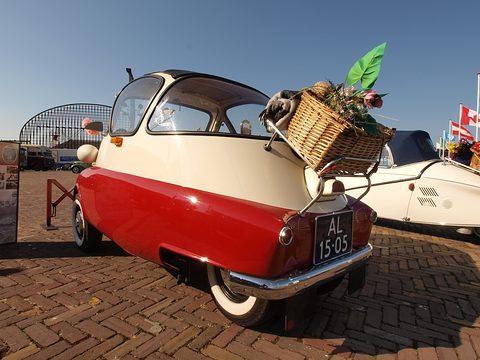 Red and cream bubble car seen from behind with a wicker basket on its rack under a blue sky. Opens a larger view