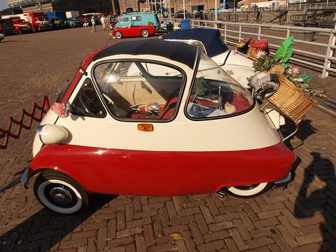 Red and cream bubble car in side view on brick paving with a wicker basket on the back. Opens a larger view