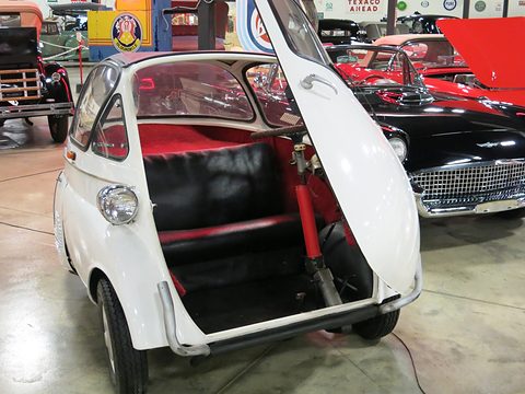 White bubble car with its front door wide open showing a black and red bench and the steering column. Opens a larger view
