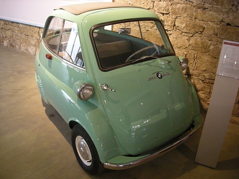 Pale green bubble car in front of a stone wall, seen from the front left. Opens a larger view