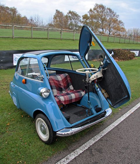 Blue bubble car on grass with its front door open and the steering wheel pulled out on its column