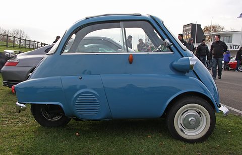 Blue bubble car in side view on grass, spectators and cars behind. Opens a larger view