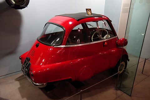 Red bubble car with a black roof behind a glass screen in a museum gallery. Opens a larger view