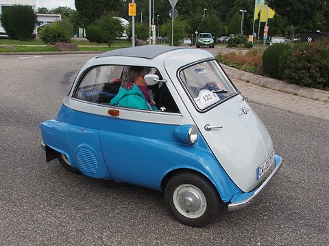 Blue and white bubble car driving on a road, a woman visible inside. Opens a larger view