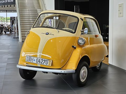 Yellow bubble car with a cream front panel seen from the front in a modern showroom. Opens a larger view