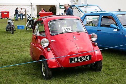 Red bubble car on grass behind a rope with a British number plate, a marquee behind. Opens a larger view