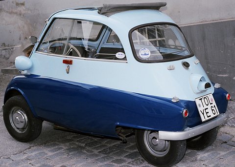 Pale and dark blue bubble car on a cobbled street with a luggage rack on its roof, seen from the front right. Opens a larger view