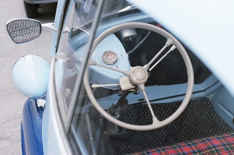 Two-spoke steering wheel mounted on the inside of the open front door, with a red tartan seat beyond. Opens a larger view