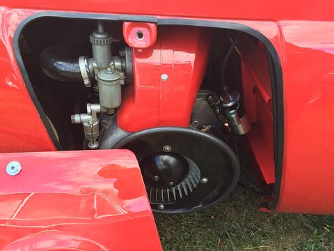 Engine with carburettor and round fan cowl visible through an opening in red bodywork. Opens a larger view