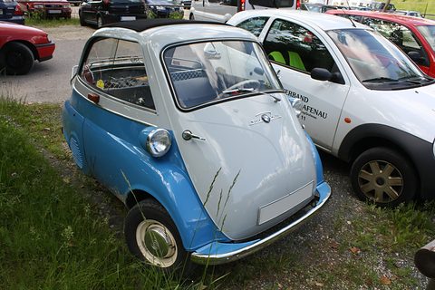 Blue and grey bubble car on grass next to a white modern car. Opens a larger view