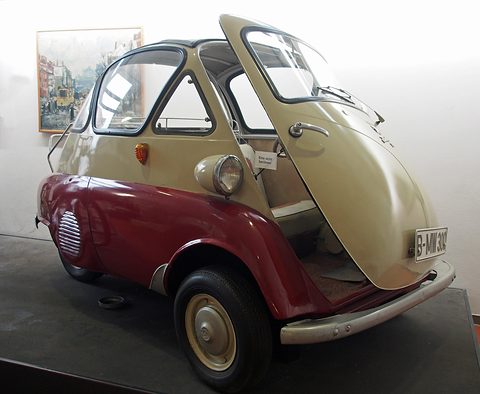 Maroon and cream bubble car with its front door open on a dark plinth before a white wall. Opens a larger view