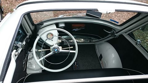 White steering wheel, gear lever and floor of a bubble car seen from above. Opens a larger view