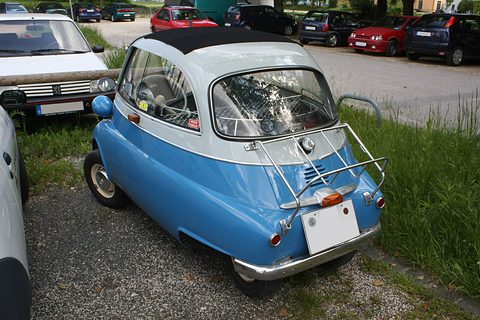 Blue and white bubble car seen from behind on grass with a luggage rack. Opens a larger view