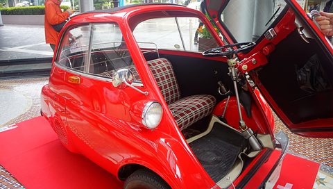 Red bubble car with its front door open, a tartan bench and the steering column inside. Opens a larger view