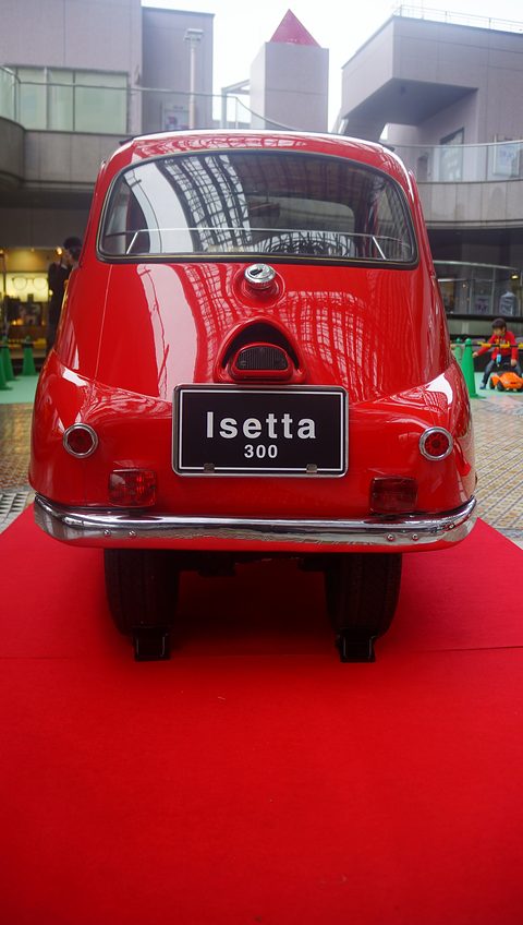 Red bubble car seen from directly behind on a red carpet, a plate reading Isetta 300. Opens a larger view