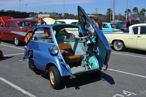 Blue bubble car with its front door open on a car park, classic American cars behind. Opens a larger view