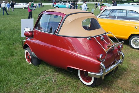Dark red bubble car seen from behind with its tan roof rolled back, on grass. Opens a larger view