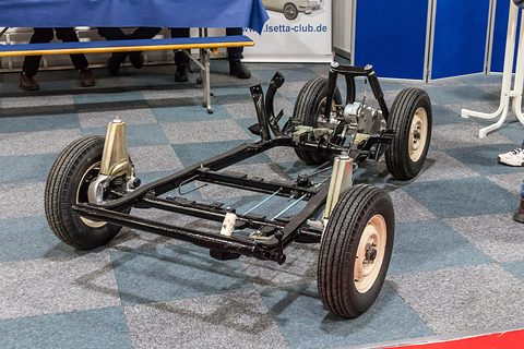 Tubular steel frame with four wheels, engine and steering column on a carpeted stand. Opens a larger view