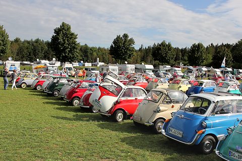 A long line of colourful bubble cars stretching across a field towards trees