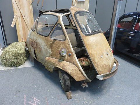 Rusty bubble car with peeling paint and its front door hanging open beside a hay bale. Opens a larger view
