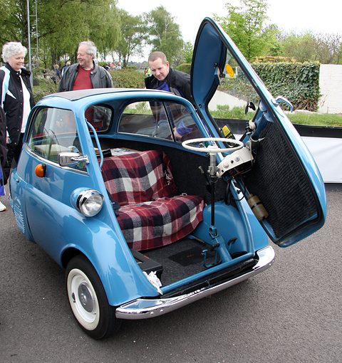 Pale blue bubble car with the front door open showing a tartan seat, people standing behind. Opens a larger view