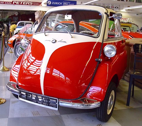 Red and white bubble car in a museum hall, posters and signs behind. Opens a larger view