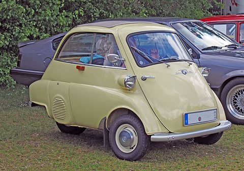 Cream bubble car parked on grass beside a dark modern car, seen from the front right. Opens a larger view