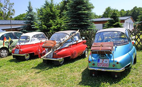 Three bubble cars parked on grass with suitcases strapped to their rear racks. Opens a larger view