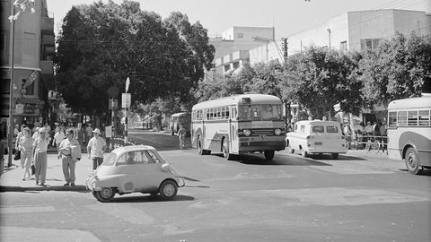 Bubble car turning at a street corner, pedestrians on the pavement and two buses and a van behind. Opens a larger view