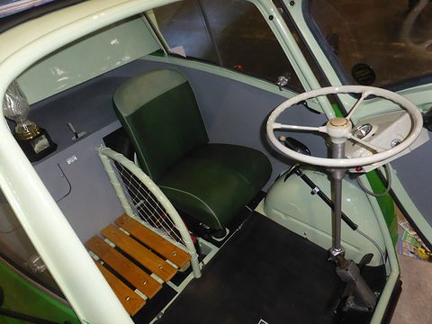 Green seat, steering wheel and a slatted wooden shelf inside a pale green cab. Opens a larger view