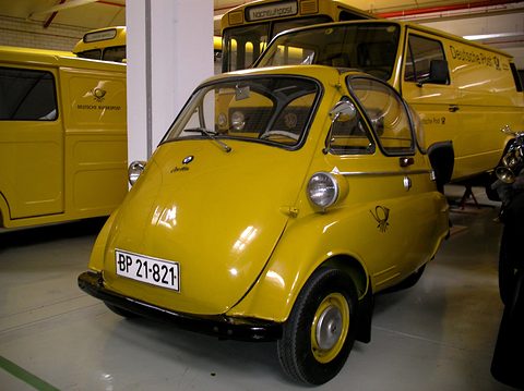 Yellow bubble car with post-office horn badges parked in front of yellow post vans. Opens a larger view