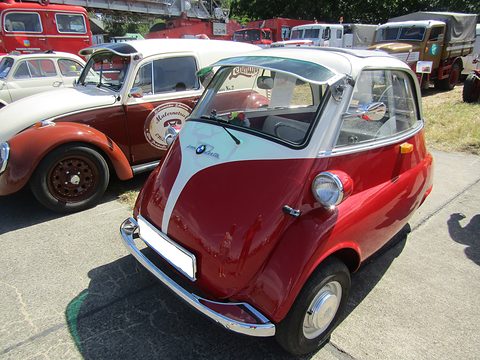 Red and white bubble car on paving, an old van and a Volkswagen behind. Opens a larger view