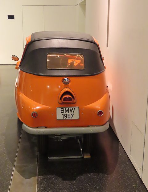 Orange bubble car from directly behind with a black fabric roof and a BMW 1957 plate. Opens a larger view