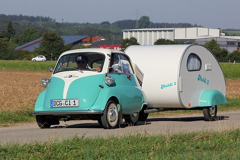 Mint green and white bubble car pulling a small white teardrop caravan on a country road. Opens a larger view