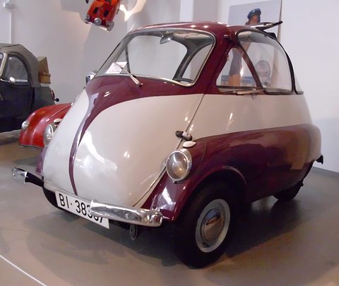 Maroon and white bubble car with a V-shaped two-tone front and Spanish number plate, seen from the front right in a museum.