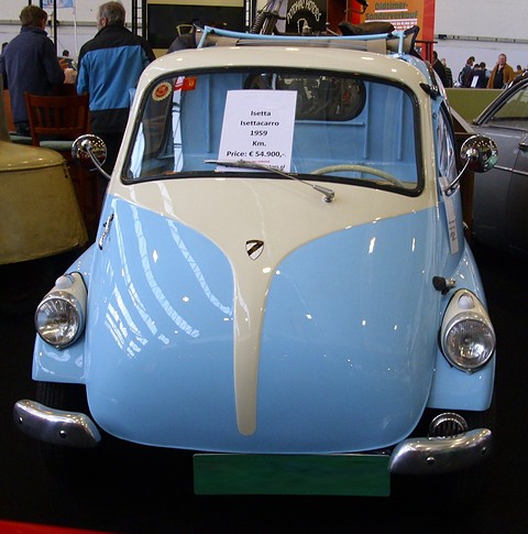 Front of a pale blue and cream truck cab shaped like an Isetta, its whole nose a door, a green plate below. Opens a larger view