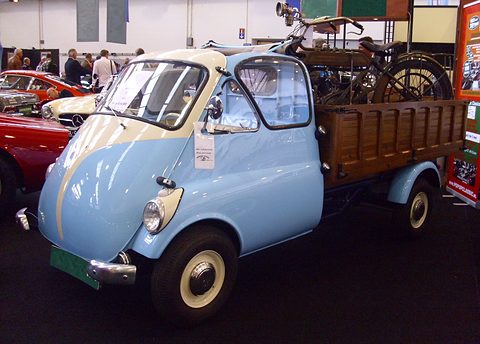 Pale blue and cream Isetta-fronted pick-up with a wooden dropside bed carrying an old motorcycle, at a show.