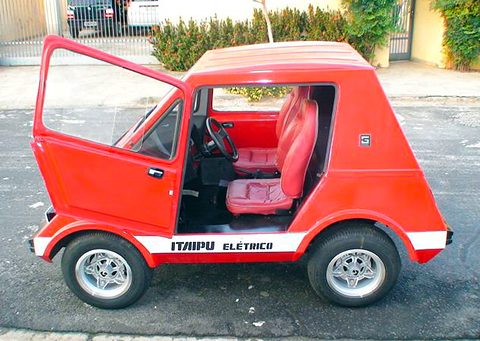 Side view of a small red trapezoid-shaped car with its large door open, red seats inside and ITAIPU ELÉTRICO on the sill.