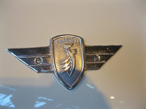 Chrome winged shield badge with the Zündapp name and emblem on cream paint. Opens a larger view