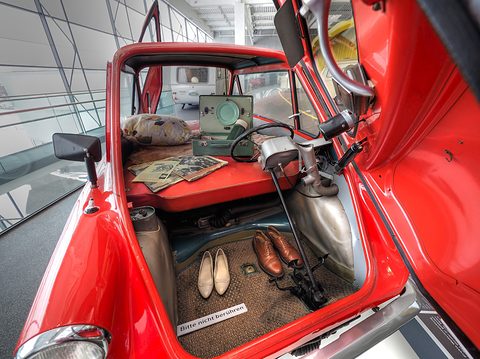 Looking in through the open front door: steering wheel, folded red seats, camping gear and shoes on the mat.