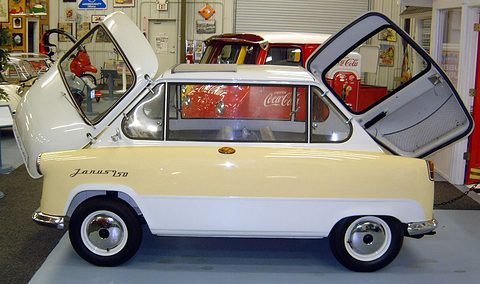 Cream and white small car in profile with its nose and tail doors swung up, a Coca-Cola cooler behind. Opens a larger view