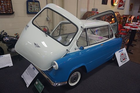 Blue and white small car with its whole nose swung up, jukeboxes and diner chairs behind. Opens a larger view