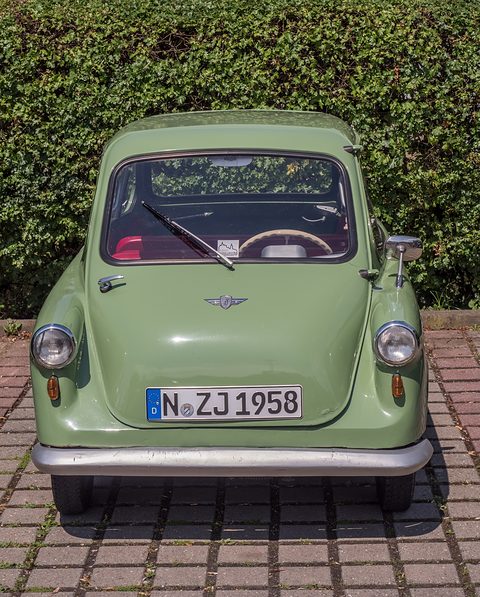 Pale green small car head-on on brick paving before a hedge, plate N ZJ 1958. Opens a larger view