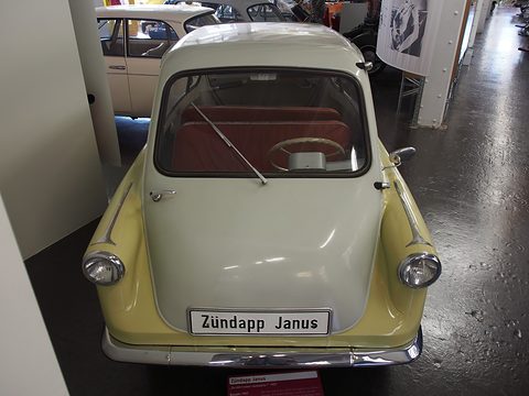 Small car facing the camera with a pale front door and yellow wings, a “Zündapp Janus” plate. Opens a larger view