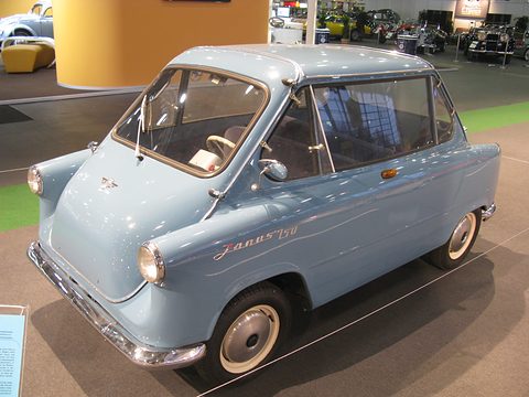 Pale blue small car with Janus 250 script and front door on a grey floor, other classic cars behind. Opens a larger view