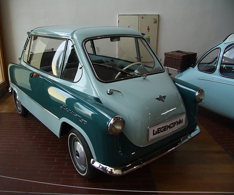 Light and dark green small car with a LEGENDY plate on a brick floor, a picnic hamper behind. Opens a larger view