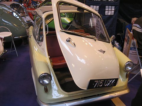 Cream small car with its whole nose swung open as a door, red seat inside, British plate 715 UXK. Opens a larger view
