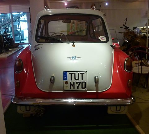 Small car seen square from behind, white upper rear door with a winged badge, plate TUT M 70. Opens a larger view