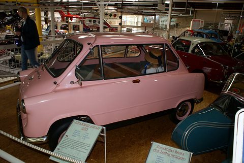 Pink small car with a hat on its seat behind an information board, a teal sidecar outfit beside it. Opens a larger view