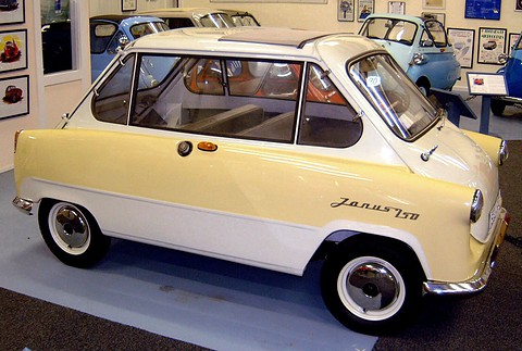 Cream and white small car in side view with Janus 250 script, a blue bubble car and framed posters behind.